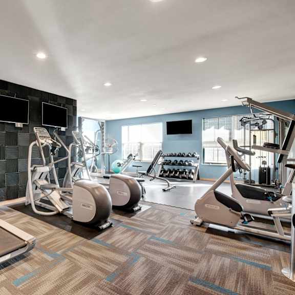 a spacious fitness center here at vue at pinnacle park with treadmills, ellipticals, strength machines, free weights, wall-mounted tvs, and large windows providing bright light for an energizing workout environment.