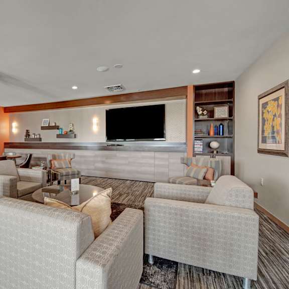a stylish resident lounge here at vue at pinnacle park with comfortable seating, a large wall-mounted tv, built-in shelving, warm wood accents, and a nearby bar-height counter for a welcoming, social gathering space.