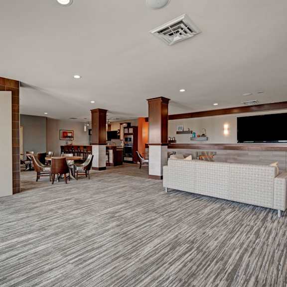 a spacious resident clubhouse here at vue at pinnacle park with open lounge seating, a modern fireplace wall, dining tables, a large tv area, and a kitchen bar space for comfortable community gatherings.