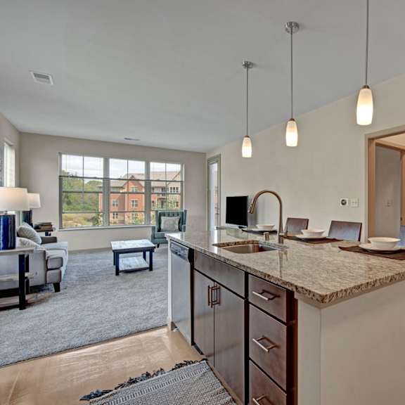 a bright open kitchen and living area here at vue at pinnacle park with a granite island, bar seating, pendant lighting, and stainless sink, flowing into a spacious carpeted lounge with large windows and natural light.