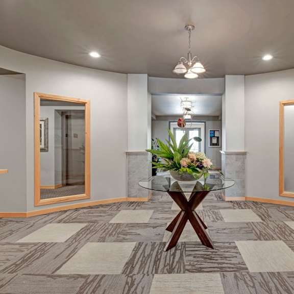 a welcoming lobby area here at vue at pinnacle park with patterned flooring, bright overhead lighting, a decorative table with floral centerpiece, and wide hall access creating a clean and inviting entrance space.