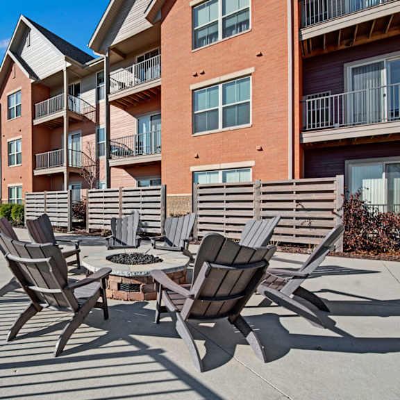 a landscaped outdoor courtyard here at vue at pinnacle park with a central fire pit, surrounding lounge chairs, paved patio space, and nearby apartment balconies creating a relaxing community gathering area.