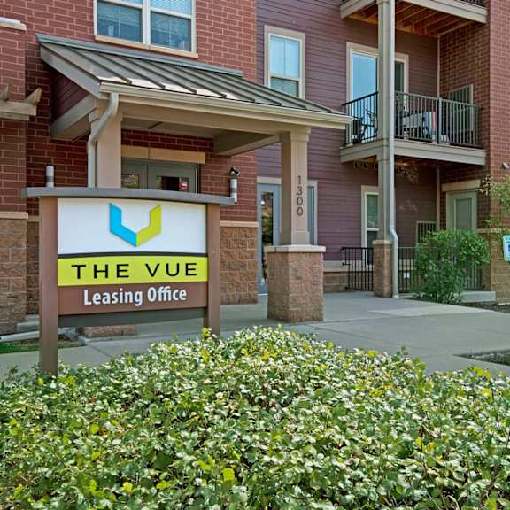 a leasing office entrance here at vue at pinnacle park with a clearly marked monument sign, covered entry, brick exterior, and landscaped greenery creating a professional and welcoming first impression.