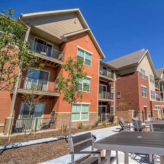 a sunny outdoor patio here at vue at pinnacle park with dining tables and chairs, nearby apartment buildings with balconies, landscaped walkways, and a pool area in view for relaxed community gathering.