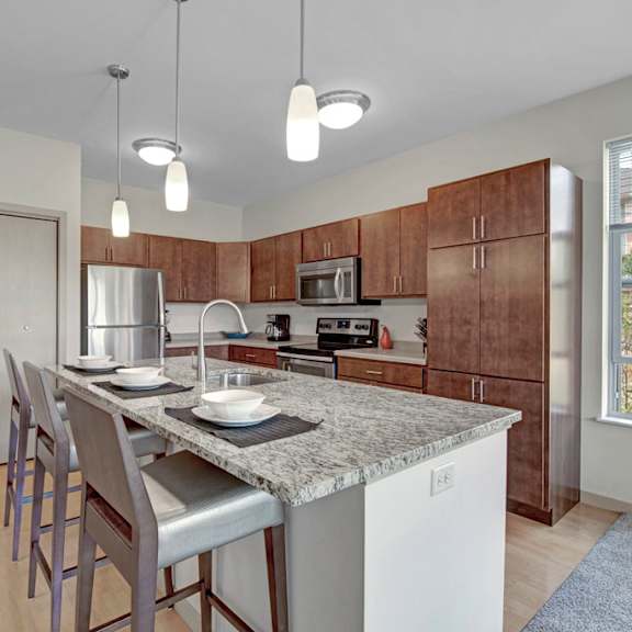 a spacious kitchen here at vue at pinnacle park with warm wood cabinets, granite countertops, stainless steel appliances, and a large island with bar seating, pendant lighting, and a bright window for natural light.