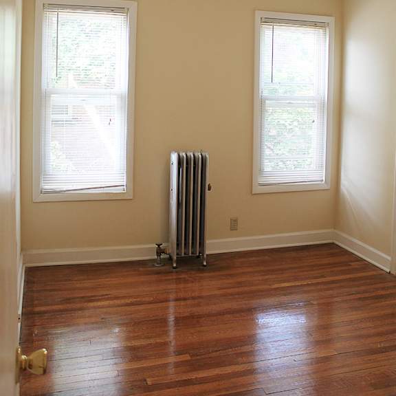 a room with a wood floor, a window with blinds, and a radiator.