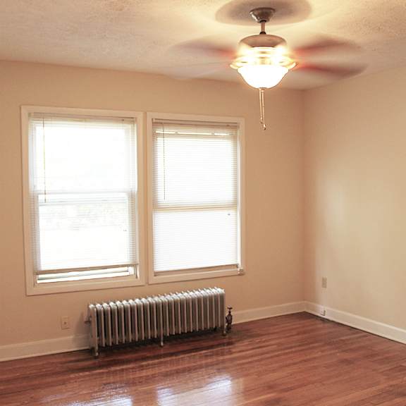 a room with a wooden floor, a ceiling fan, and a radiator.