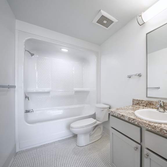 a white bathroom with a granite counter top and a white toilet.