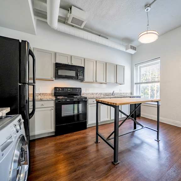 a black fridge is on the left of a kitchen with a black oven and a black microwave.