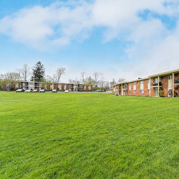 a grassy field in front of a brick building with cars parked in the background at integrity chardon apartments,ohio, 44024