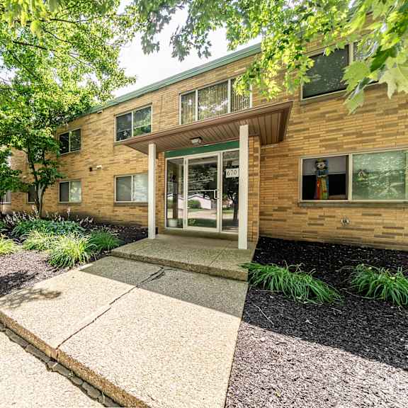 a building with a brown wooden exterior and a glass door is surrounded by greenery.
