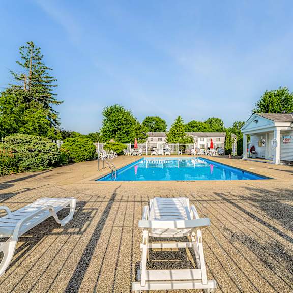 a pool surrounded by white chairs and a wooden deck.