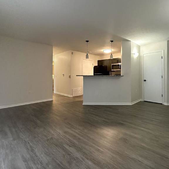 an empty living room with a kitchen in the background