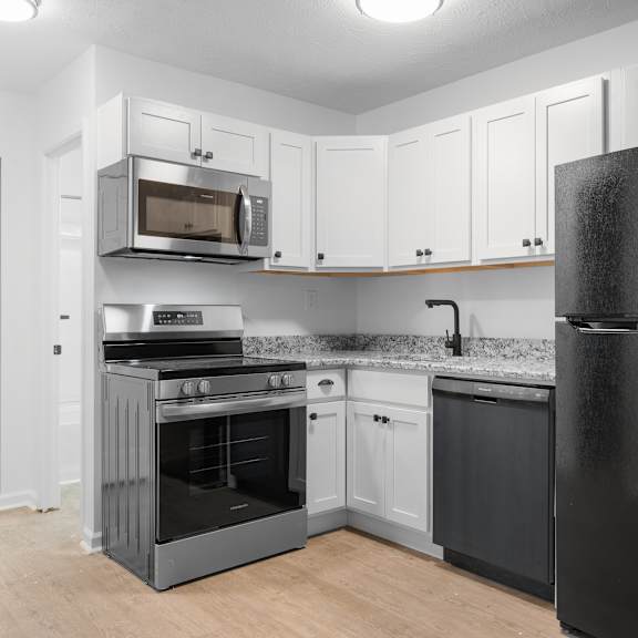 a black refrigerator stands in a kitchen with white cabinets and a black stove.