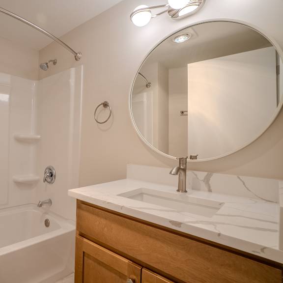 a white bathroom with a round mirror and a white sink t atrium in the village, beachwood