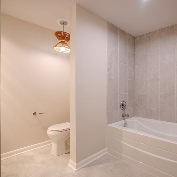 a white bathroom with a toilet, tub, and a light fixture t atrium in the village, beachwood