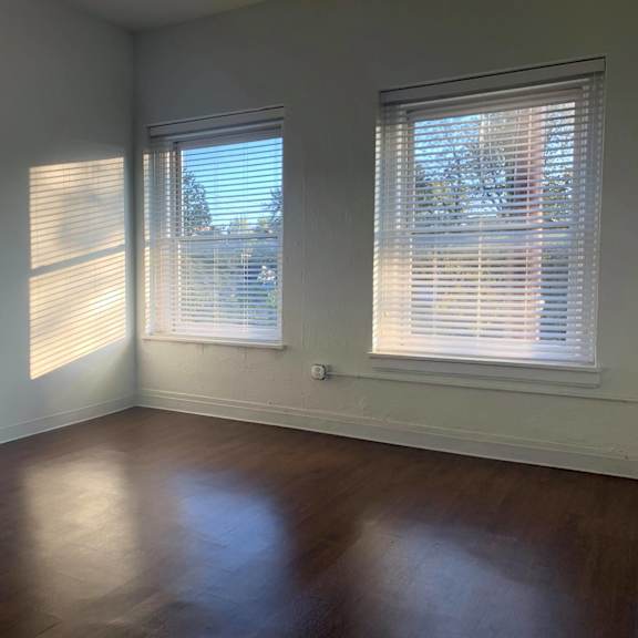 a room with wooden floors and two windows with blinds.