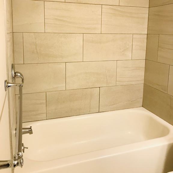 updated bathtub with stainless steel accents and large stone wall tiles