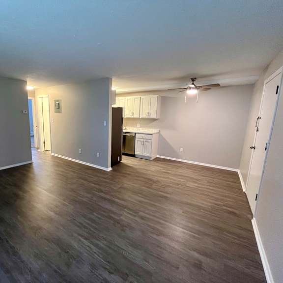 an empty living room with wood floors and a kitchen