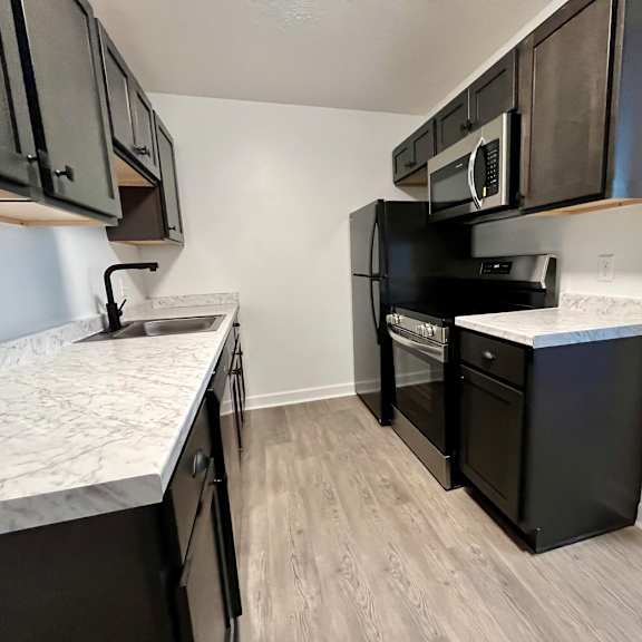 an empty kitchen with black appliances and marble counter tops