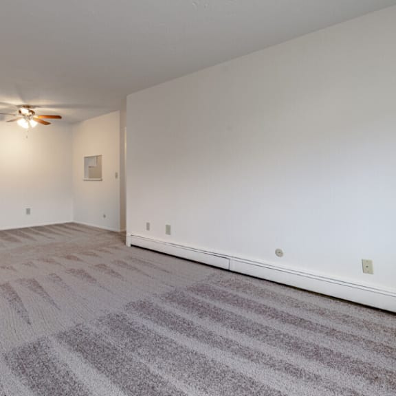 the living room and dining room of an apartment with carpet and a ceiling fan