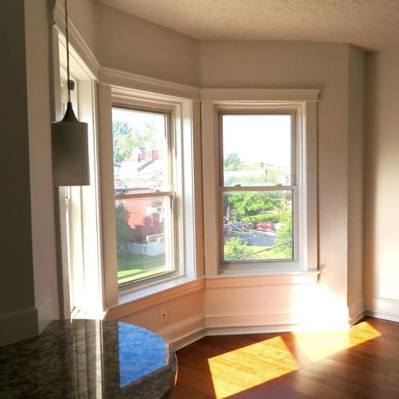 a sunny room with a large window and a view of a red building outside.