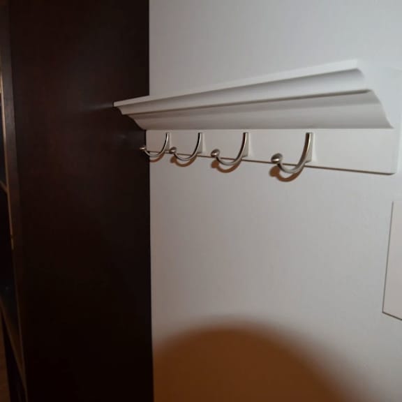 a white shelf with three hooks is mounted on a white wall.