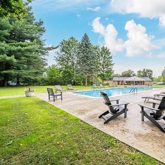 a pool surrounded by lawn chairs and trees.
