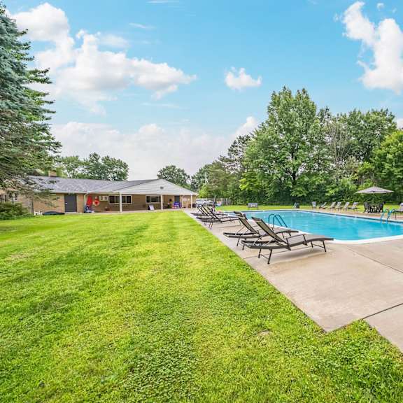 a pool surrounded by lawn chairs and trees.