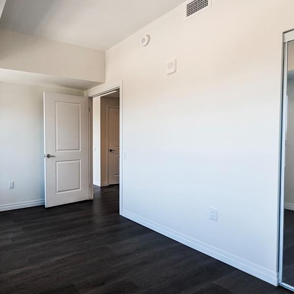 a spacious room with white walls and dark wood flooring.