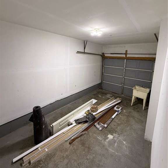 a room with a white wall and a grey floor with a lot of tools and wood planks.