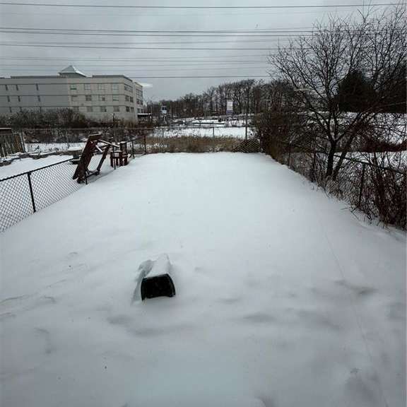 a snow-covered landscape with a fence and a building in the distance.