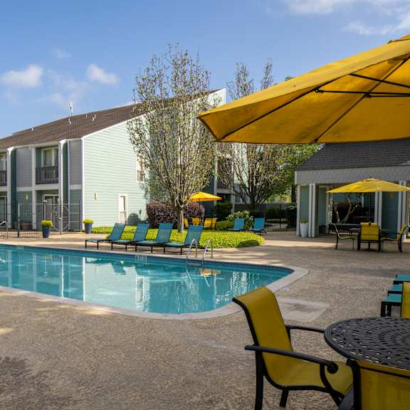 a pool area with chairs and umbrellas in front of a building.