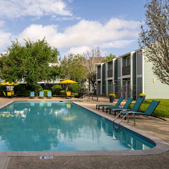 a small pool surrounded by lawn chairs and trees.