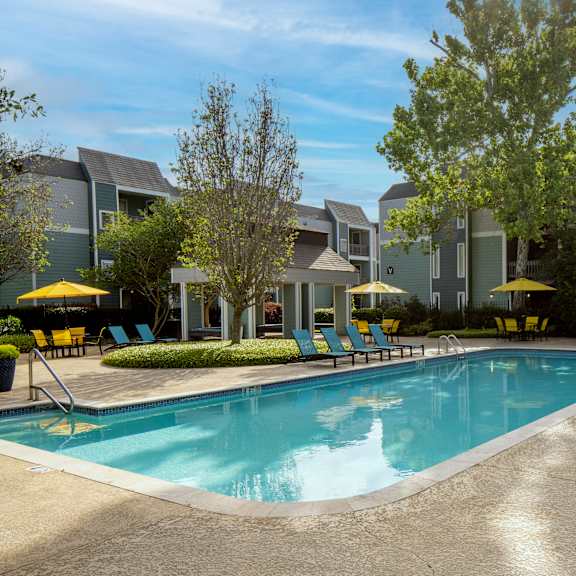 a swimming pool surrounded by lounge chairs and umbrellas in front of a building.