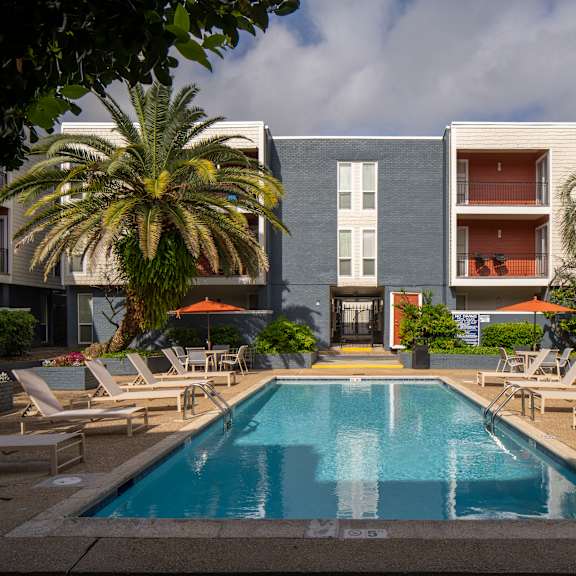 a swimming pool surrounded by lounge chairs and palm trees in front of a modern apartment building.