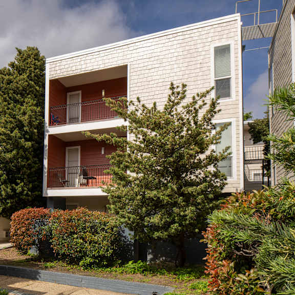 a white building with balconies is surrounded by greenery.