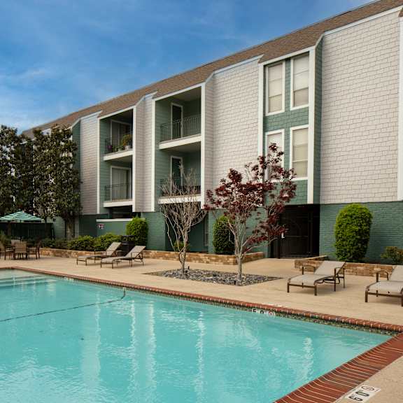 a swimming pool in front of a building with a green tree.