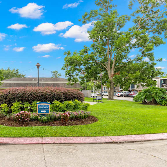 a sign in a grassy area with a tree and a building in the background.