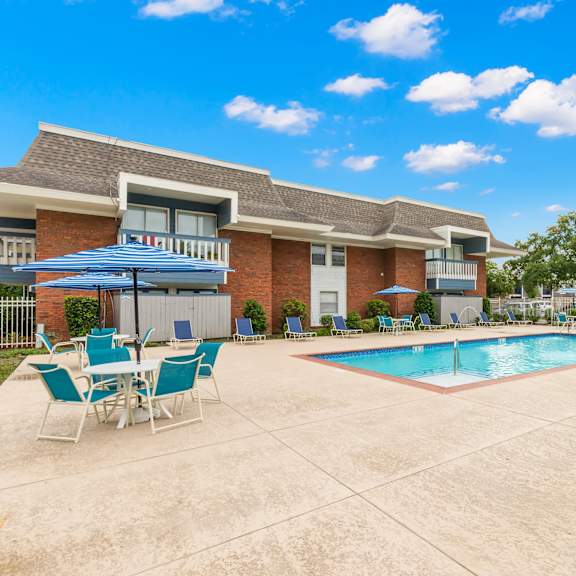 a pool area with chairs and a building in the background.