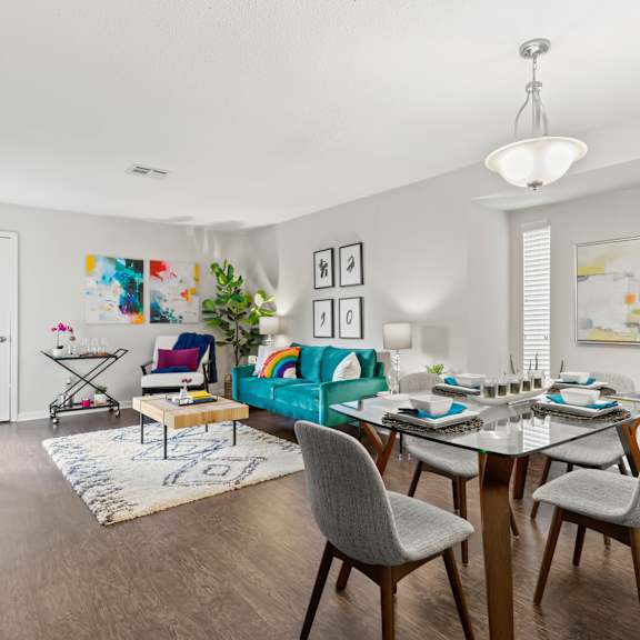 a dining room with a table set for six and a couch with a green throw pillow.