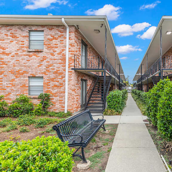 a row of red brick houses with green bushes and a walkway in between.
