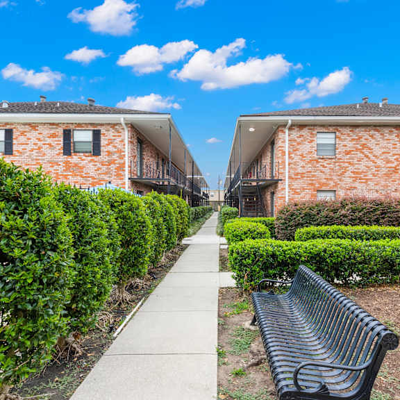a black bench is situated on a concrete path between two red brick buildings.