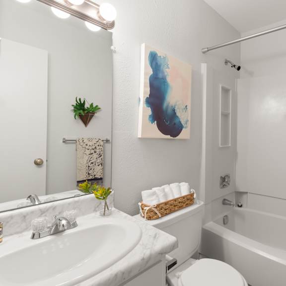 a bathroom with a white tub, pink shower curtain, and a painting on the wall.