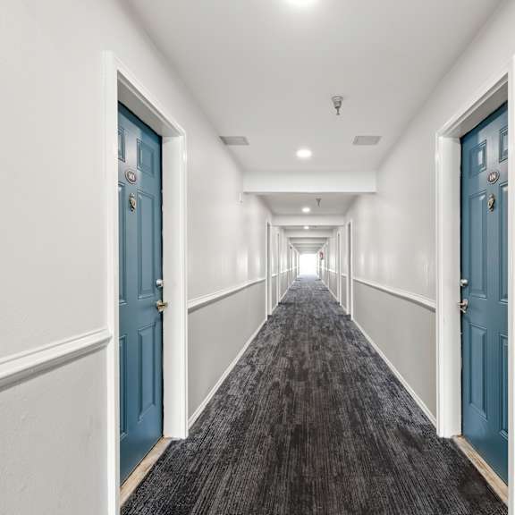 a long hallway with blue doors and carpeted flooring.