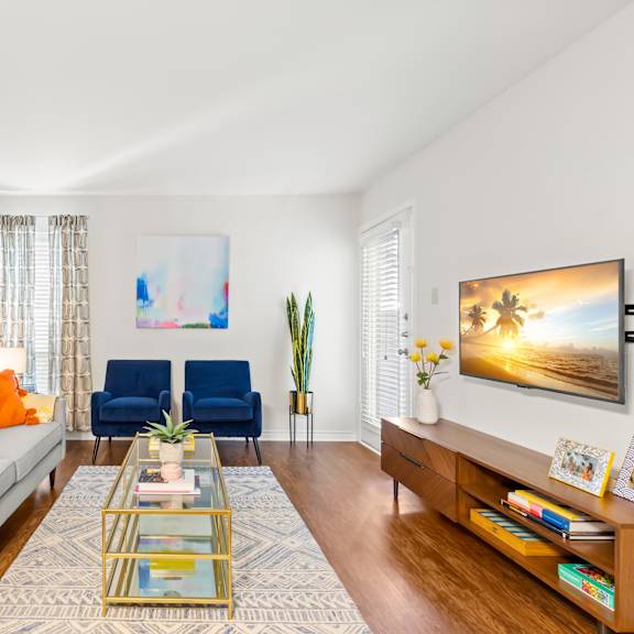 a living room with a grey couch, a blue chair, a glass coffee table and a painting on the wall.