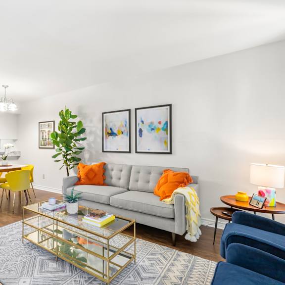 a living room with a grey couch, yellow chairs, and a glass coffee table.