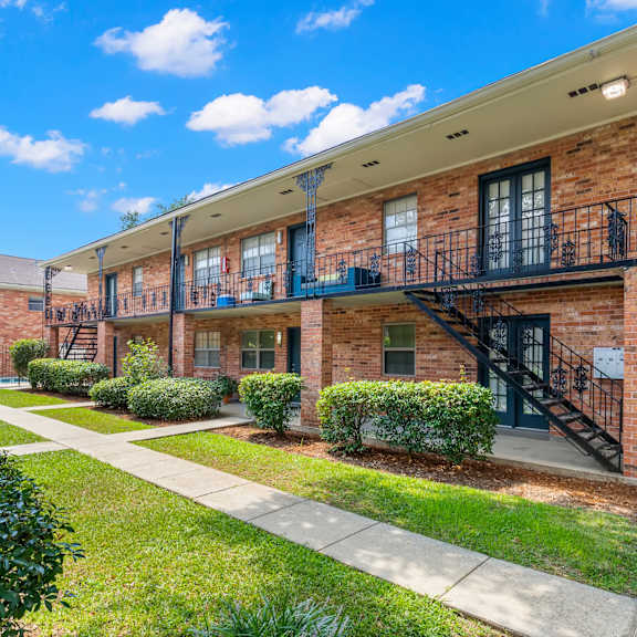 a sunny day at a brick apartment complex with green bushes and a clear blue sky.