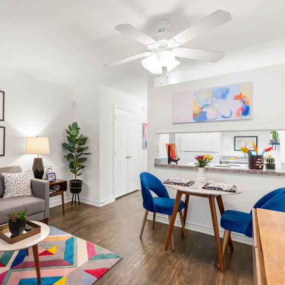 a living room with a grey couch, a coffee table, a dining table with chairs, a ceiling fan, and a painting on the wall.