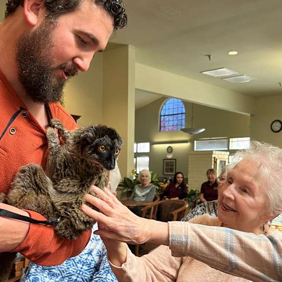 a man holding a small animal while an older woman reaches out to touch it.